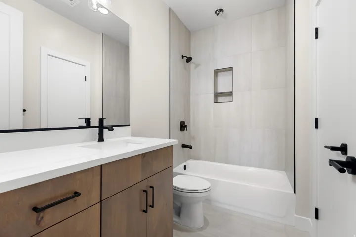 Bathroom featuring a wood-finish vanity with a white countertop and integrated sink, matte black faucet, and rectangular mirror