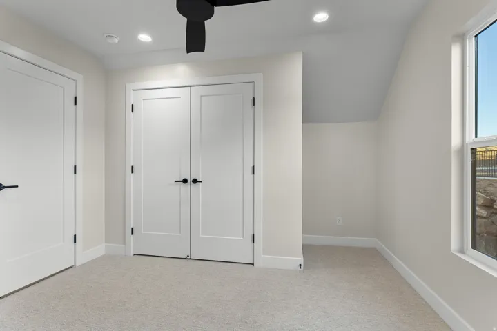 Neutral-toned room featuring a window, light-colored carpet, recessed lighting, and a dark-toned ceiling fan