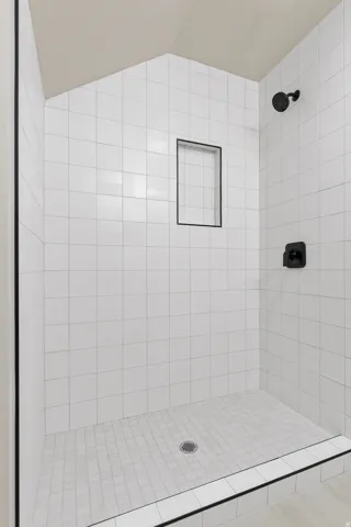 Walk-in shower featuring white subway tile walls, a built-in shower niche with dark trim, dark shower fixtures, and a white mosaic tile shower pan