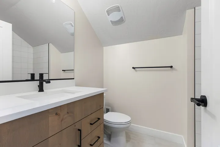 Bathroom featuring a wood-finish vanity with a white countertop and integrated sink, matte black faucet, and a large wall-mounted mirror