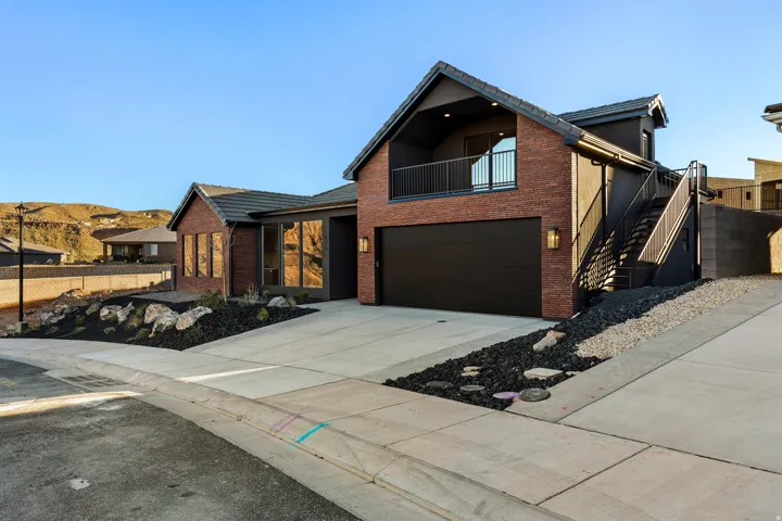 Modern exterior featuring a prominent black garage door, red brick accents, and a second-story balcony with black railing