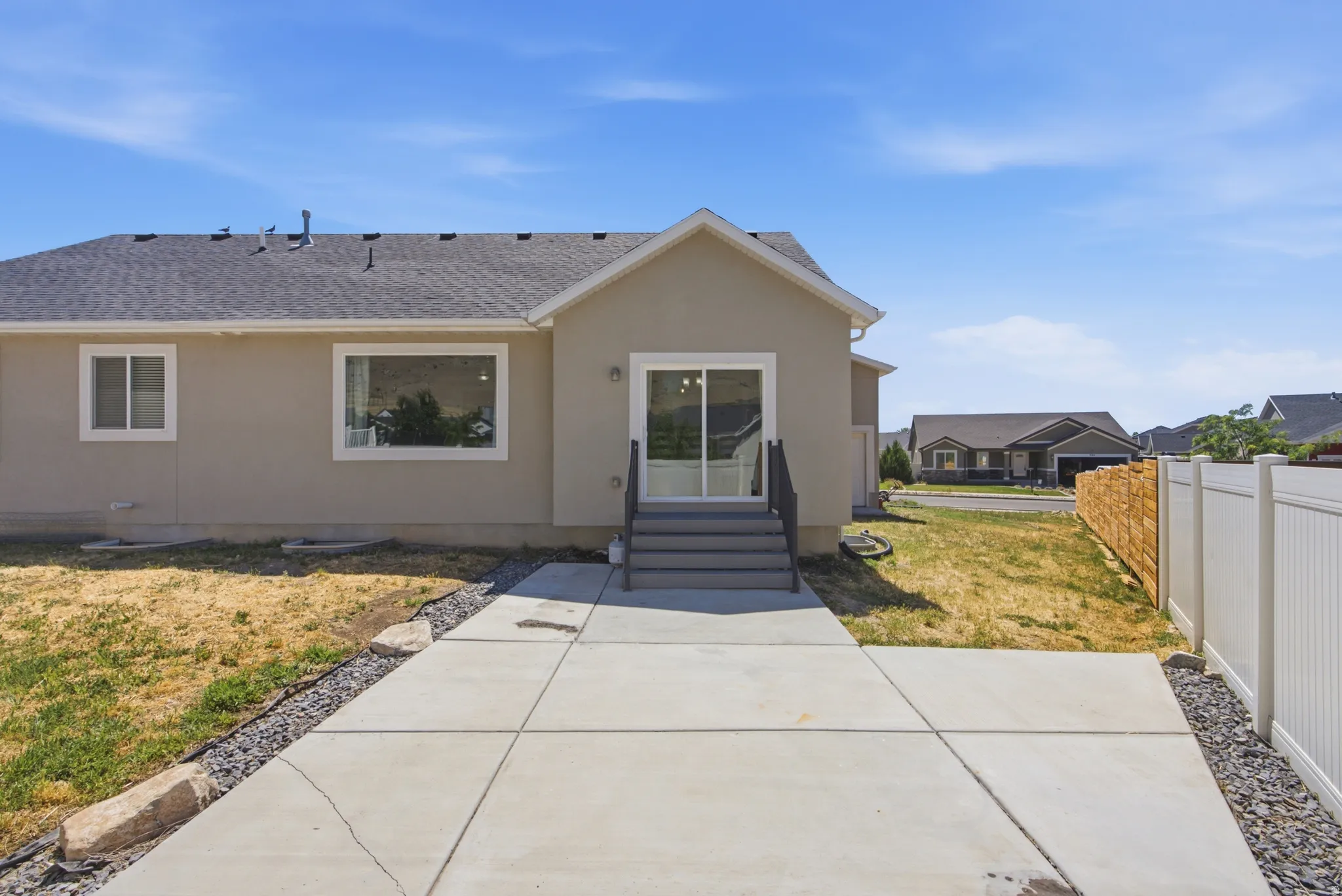Rear exterior featuring a sliding glass door with integrated blinds, concrete patio, and steps with dark railings