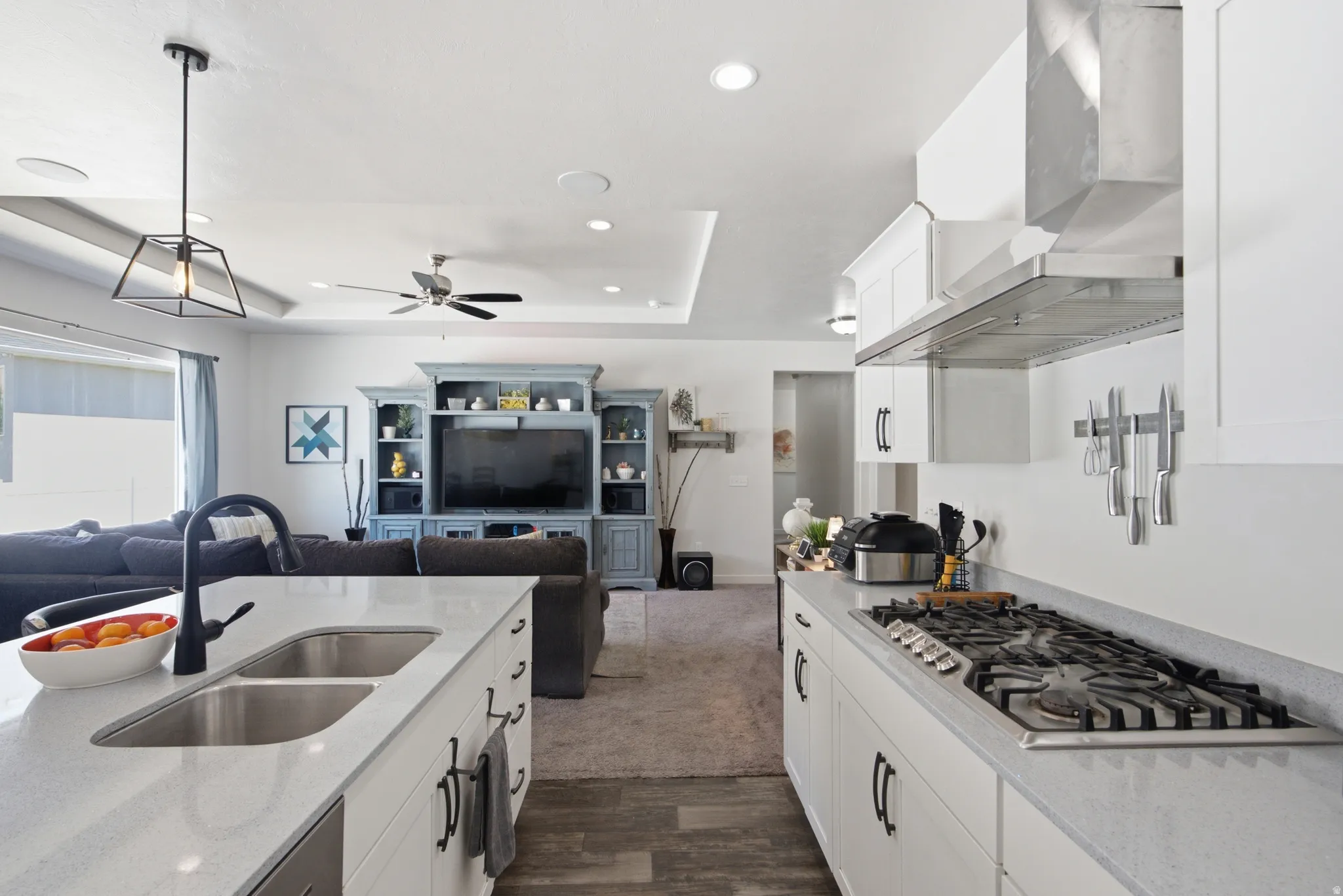 Open-concept living space featuring a kitchen island with dual basin sink and a gas cooktop with a stainless steel range hood