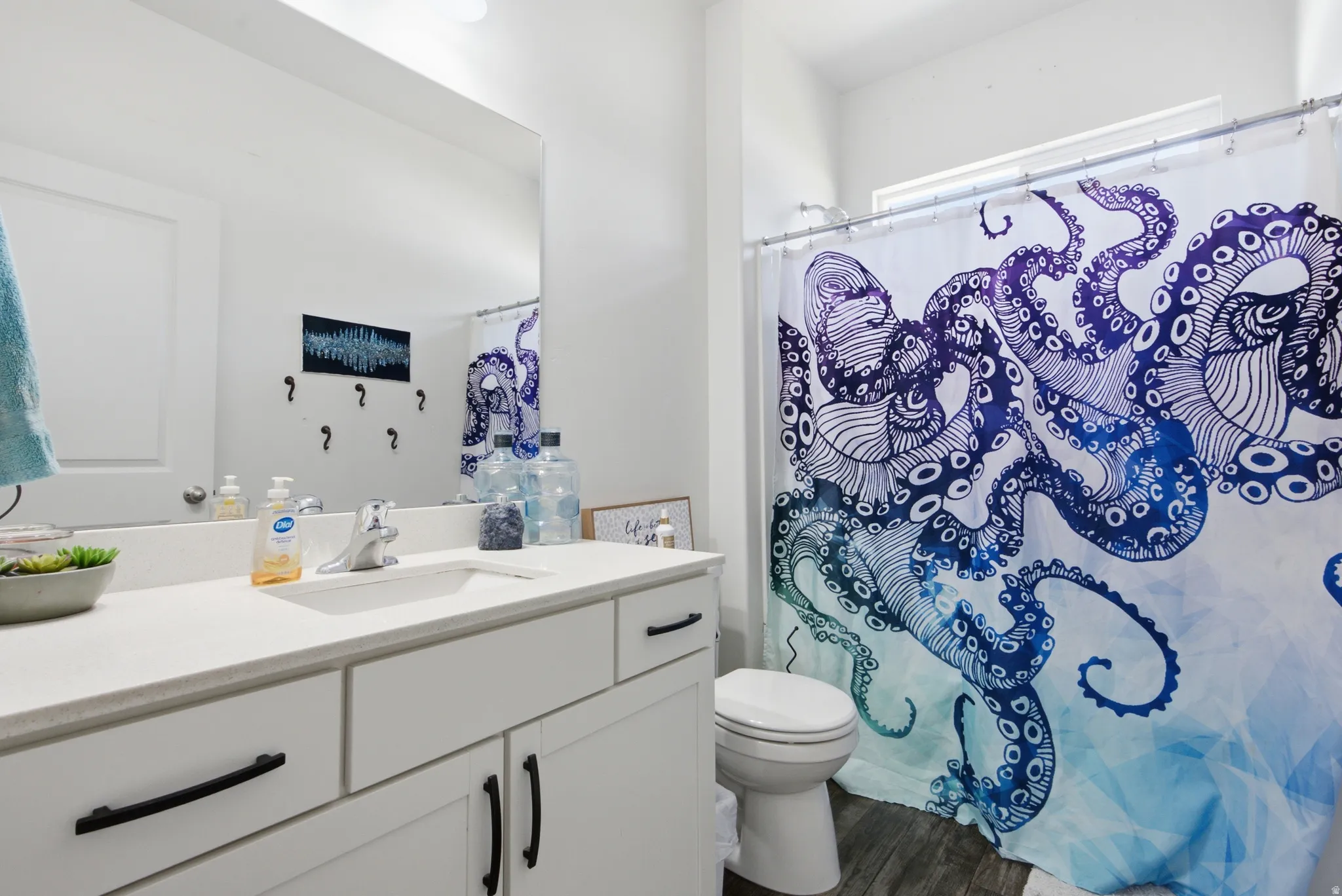 Bathroom featuring a vanity with a white countertop and dark hardware, a large wall-mounted mirror, and wood-finish flooring