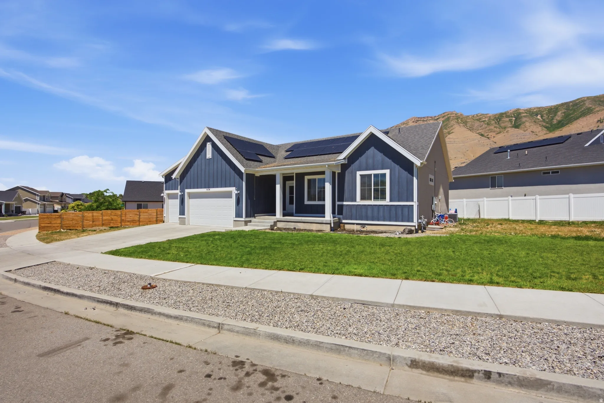 Contemporary ranch-style residence featuring blue vertical siding, a white-trimmed gable, a covered entry porch, a two-car garage, and a landscaped front lawn