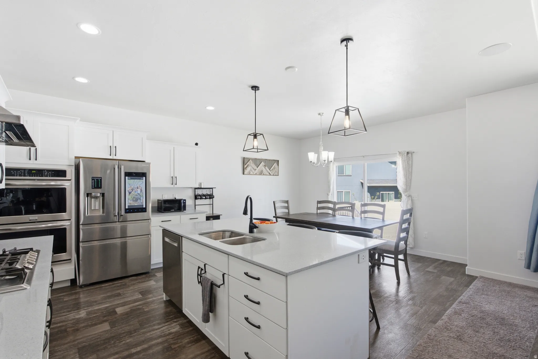 Bright kitchen featuring white cabinetry, stainless steel appliances, a center island with sink, and wood-finish flooring