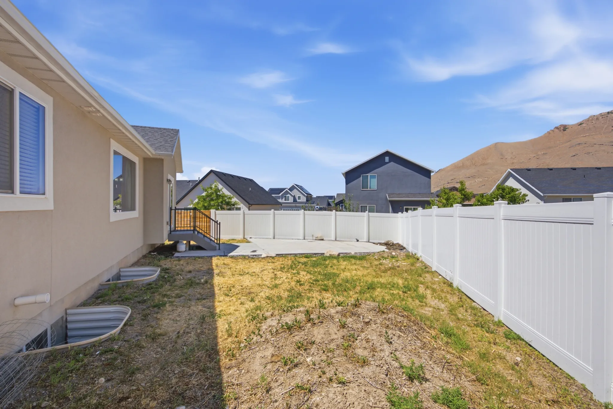 Spacious backyard featuring a concrete patio, a private deck with stairs, and a white vinyl privacy fence
