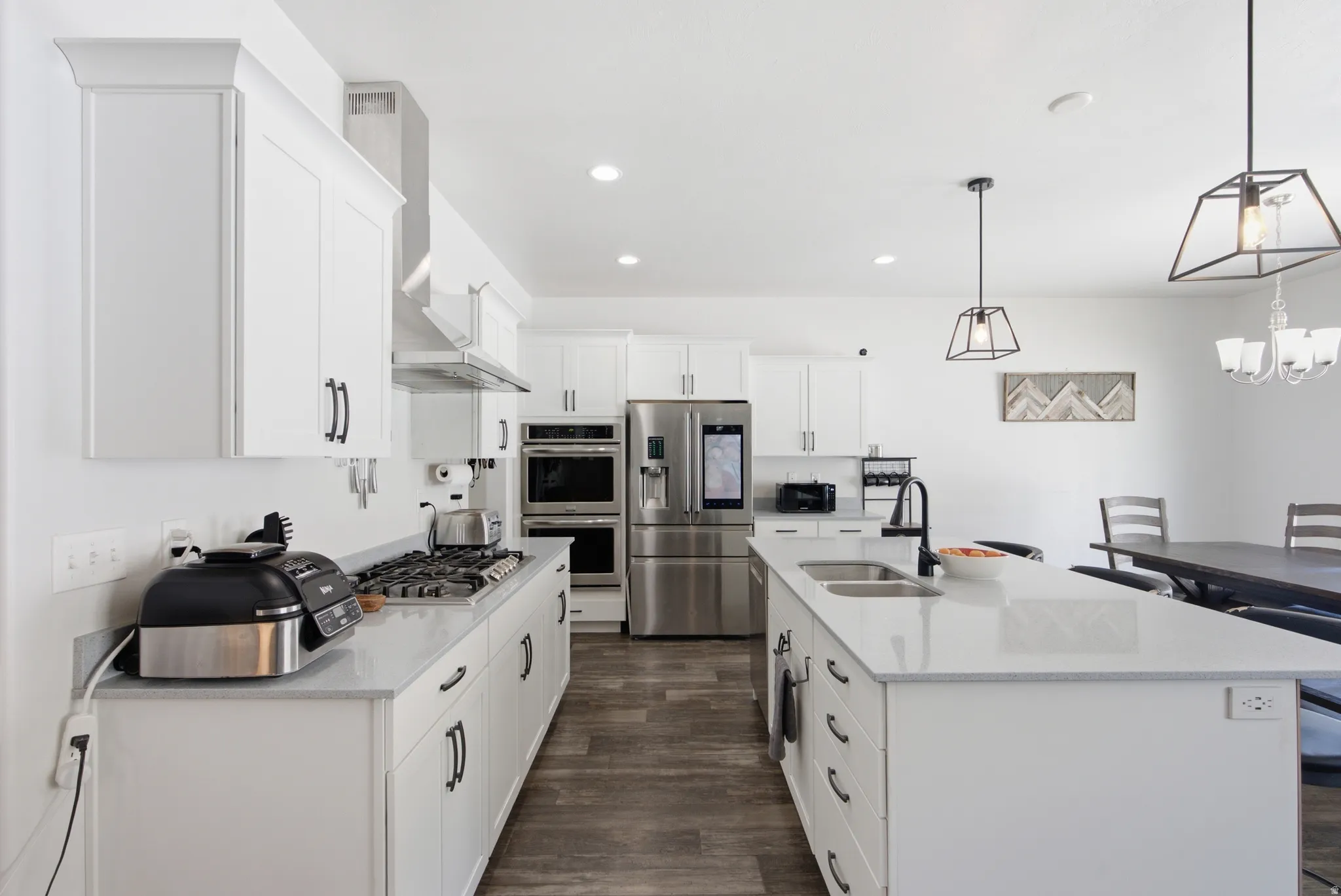 Contemporary kitchen featuring white cabinetry, light-toned countertops, stainless steel appliances, a center island with a double sink, and wood-finish flooring