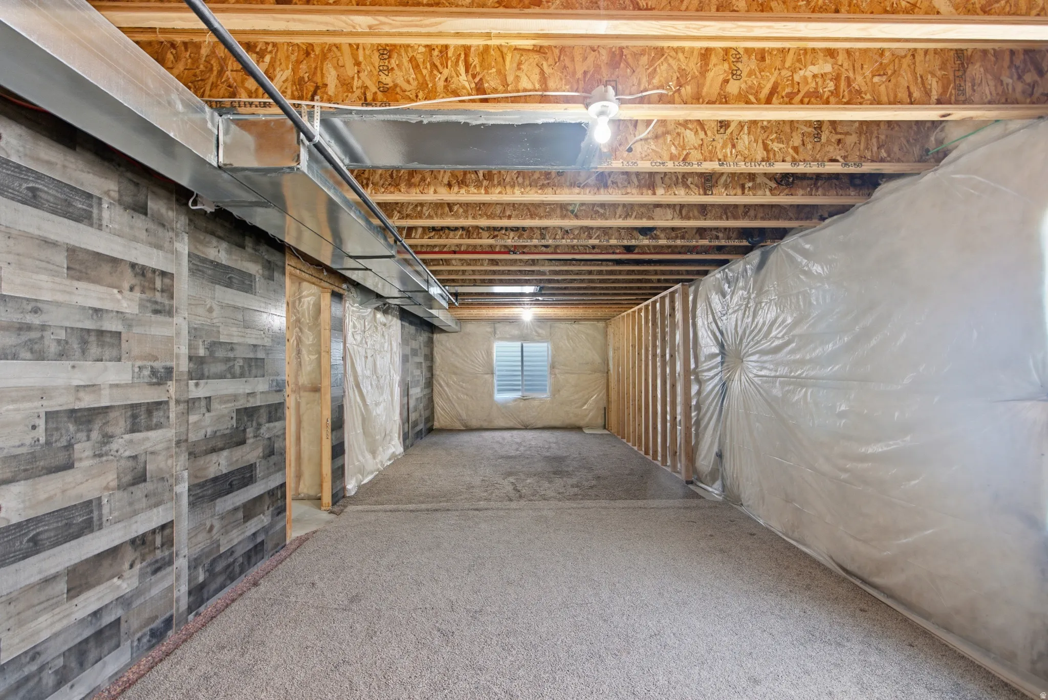 Unfinished basement featuring exposed wood joists, a textured wall treatment, and a framed room with a window