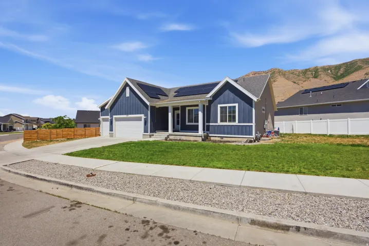 Contemporary ranch-style residence featuring blue vertical siding, a white-trimmed gable, a covered entry porch, a two-car garage, and a landscaped front lawn