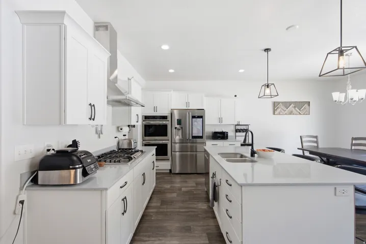 Contemporary kitchen featuring white cabinetry, light-toned countertops, stainless steel appliances, a center island with a double sink, and wood-finish flooring