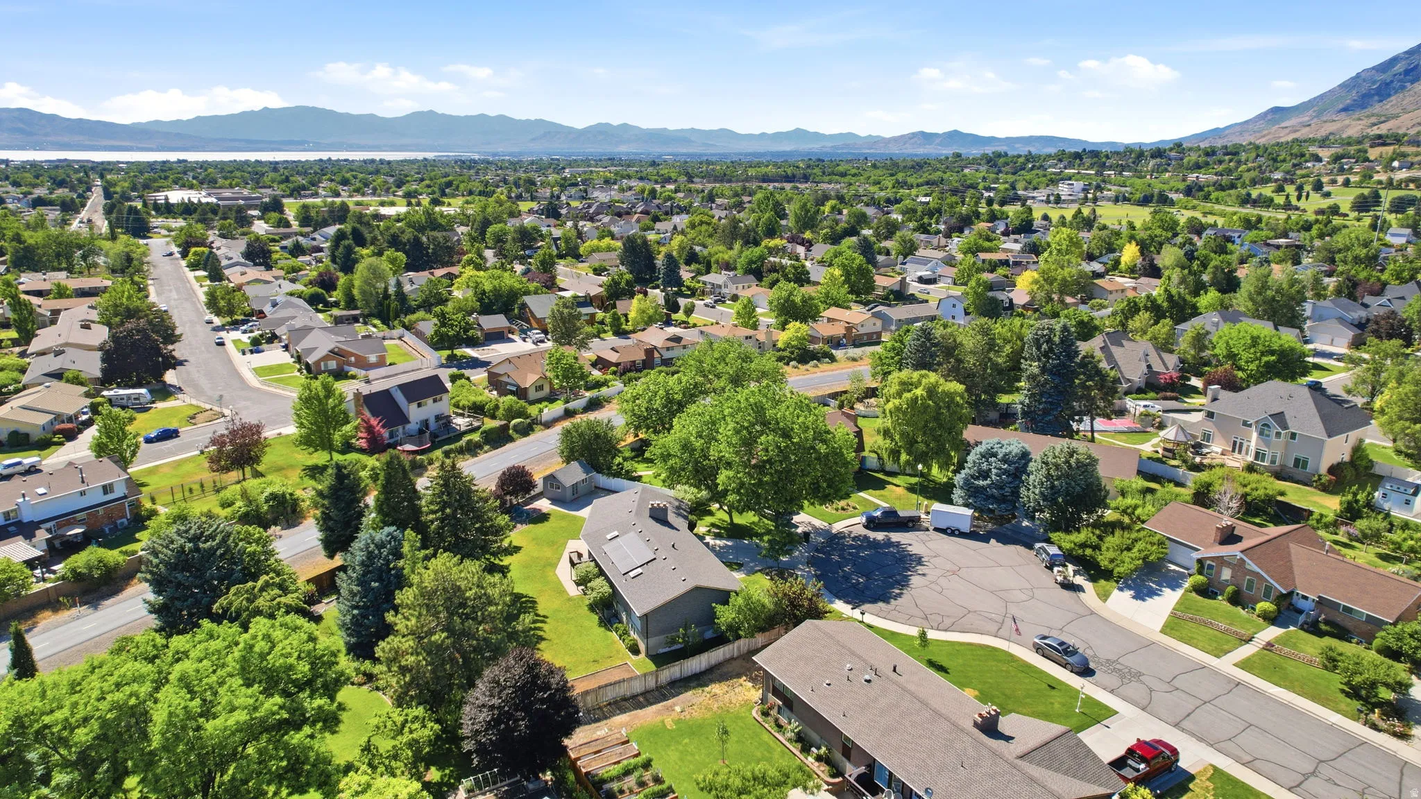 Expansive residential area featuring established homes, mature trees, paved streets, and mountainous terrain