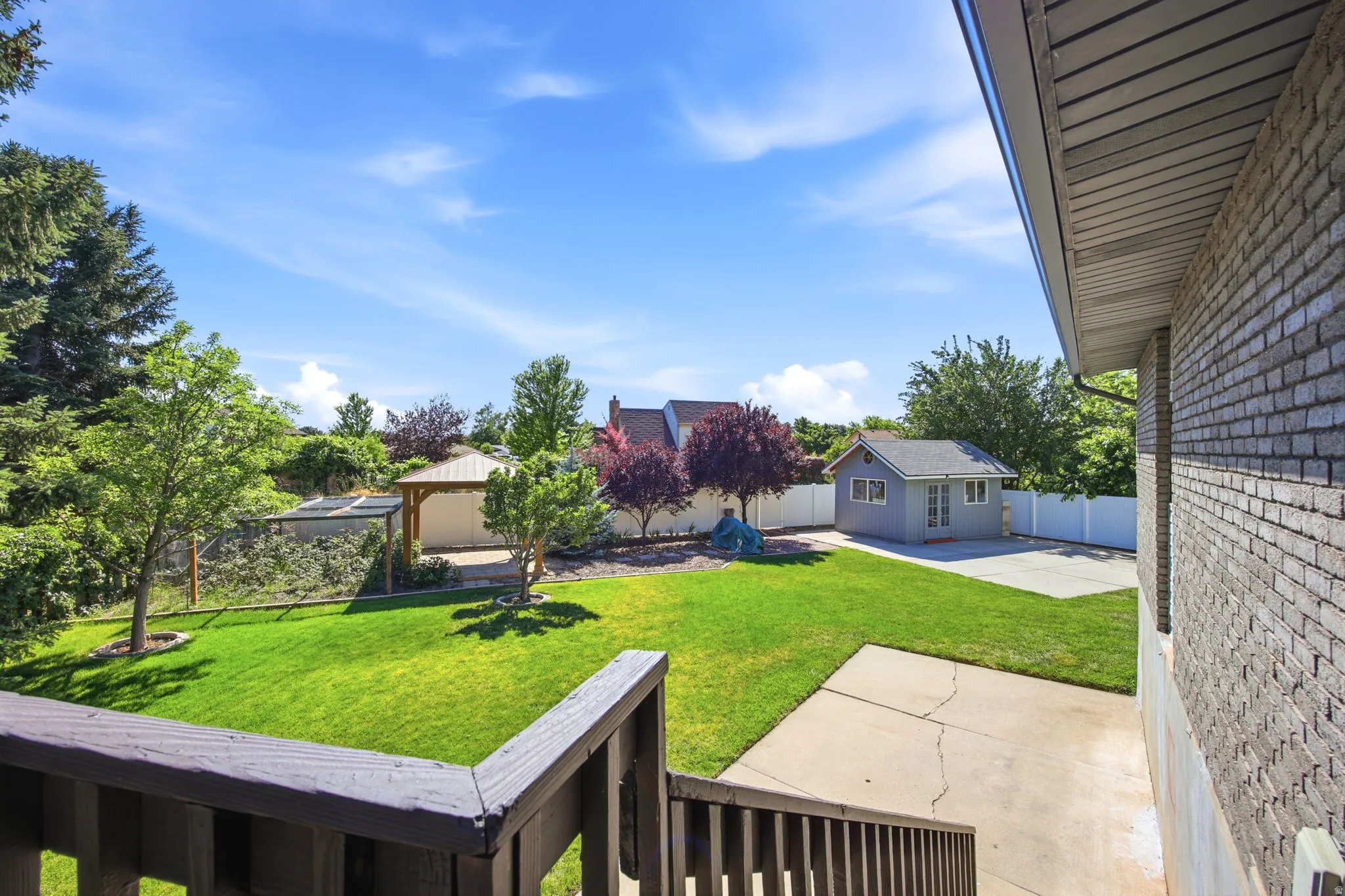 Expansive backyard featuring a lush lawn, mature trees, a detached storage shed, a paved patio area, and a covered gazebo