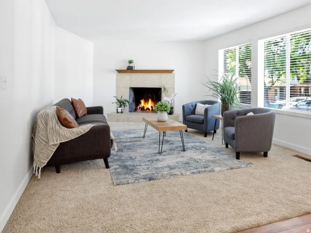 Living area featuring a stone-clad fireplace with a wood mantel, broad windows, and a combination of wood-finish flooring and carpeting