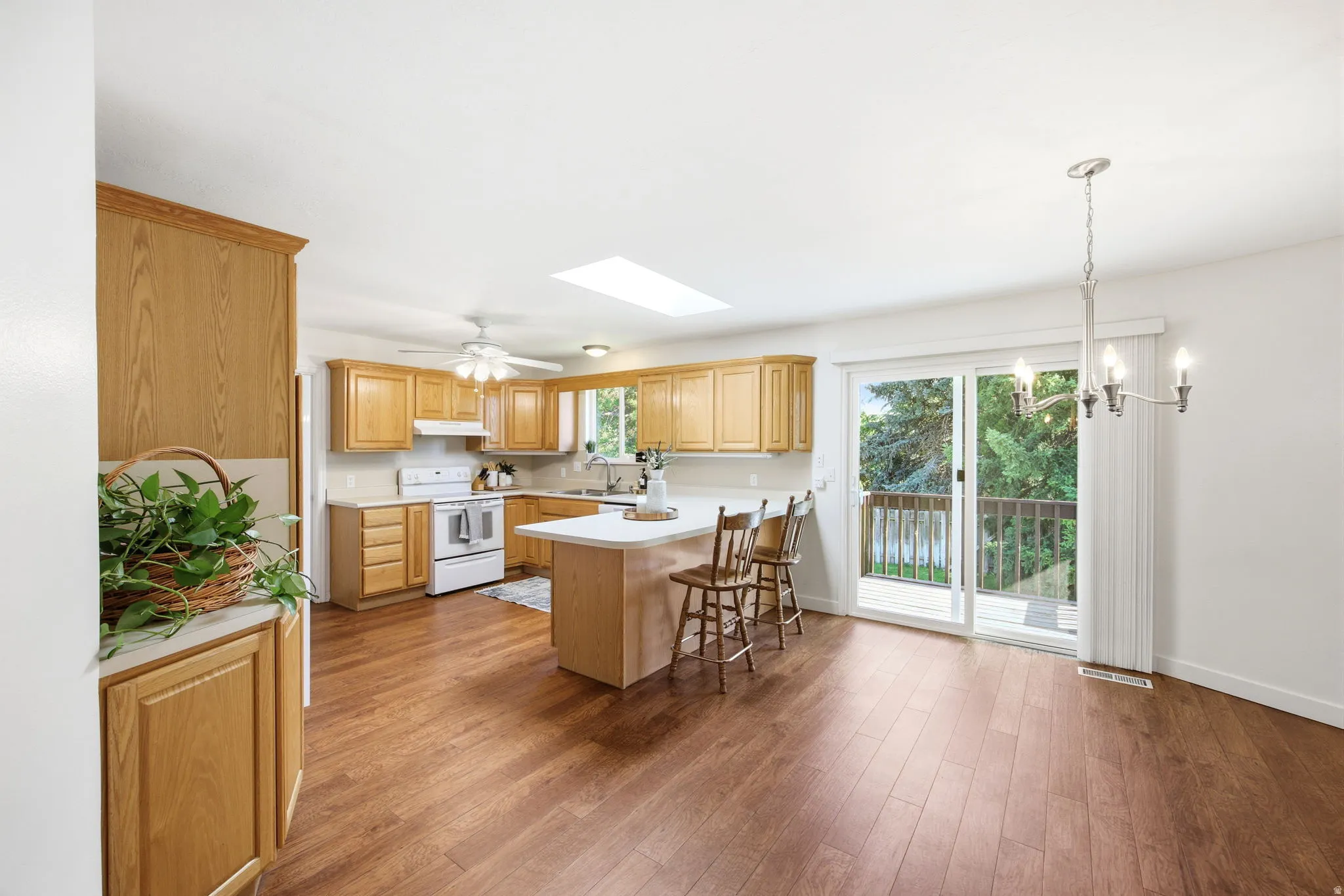 Open-concept kitchen and dining area featuring wood-finish flooring, ample cabinetry with light wood finishes, a kitchen island with seating, a skylight, and direct access to an exterior deck through a sliding glass door