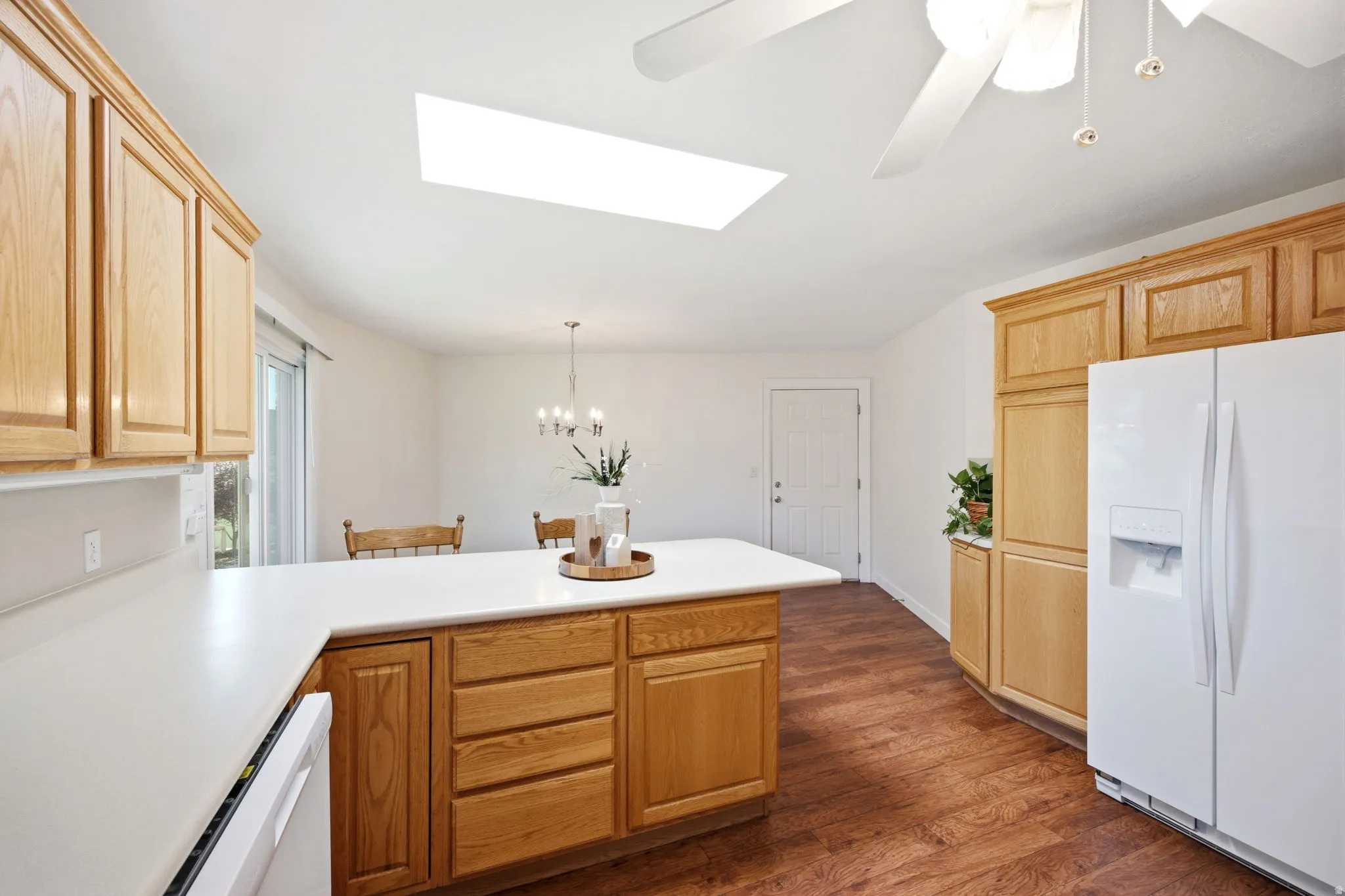 Spacious kitchen featuring a skylight, wood-finish flooring, light wood cabinetry, white countertops, and a white appliance suite