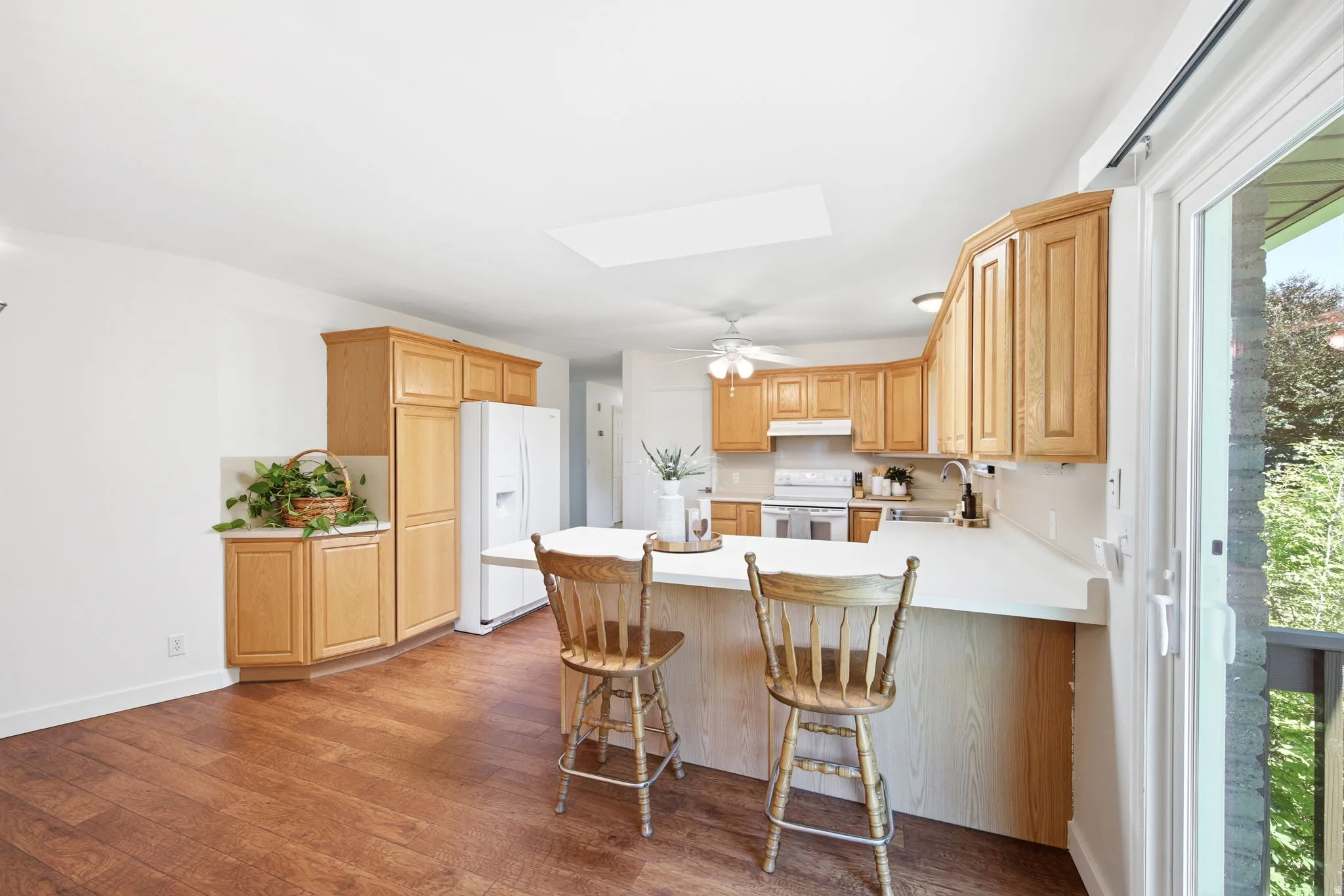 Open-concept kitchen featuring wood-finish flooring, light wood cabinetry, white countertops, a built-in kitchen island with seating, and a large sliding glass door