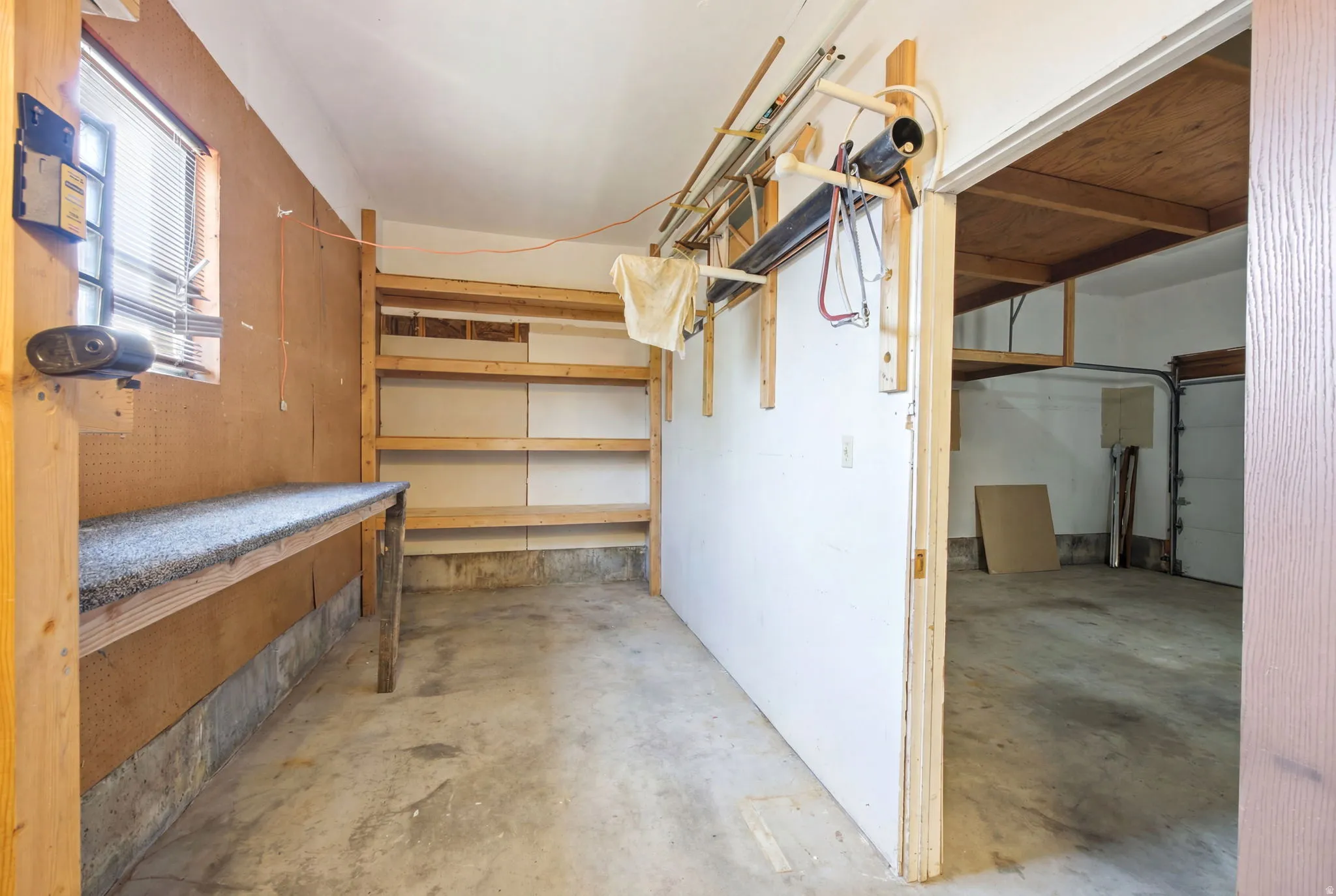 Utility space featuring a workbench with a textured surface, a window with blinds, and built-in wooden shelving for storage