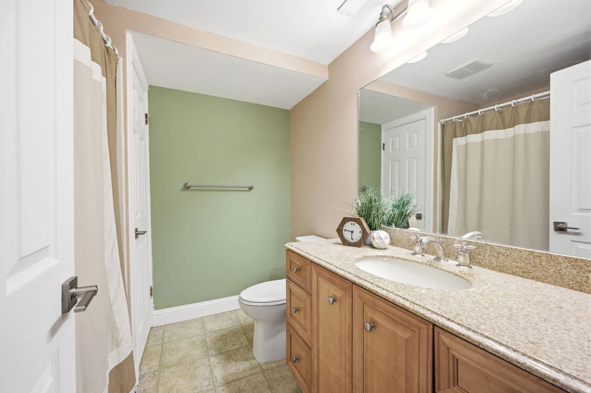 Bathroom featuring a light wood-finish vanity with an undermount sink, a speckled countertop, and a large wall-mounted mirror