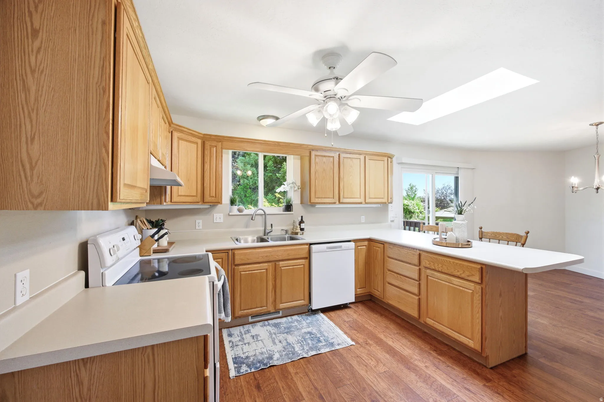 Kitchen featuring wood-finish flooring, wood cabinetry, white countertops, and white appliances