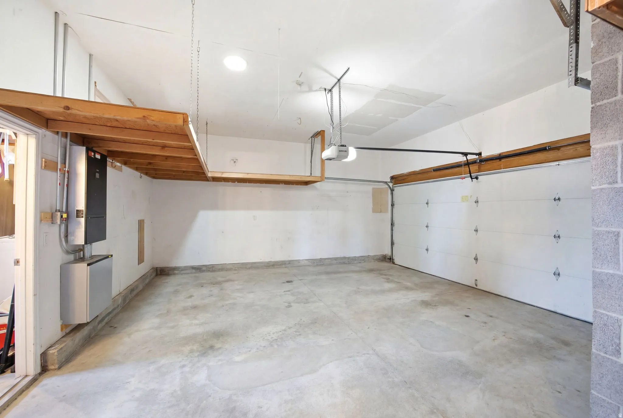 Spacious garage featuring concrete flooring, an automatic garage door opener, overhead wood-finish storage shelving, and a wall-mounted hot water heater