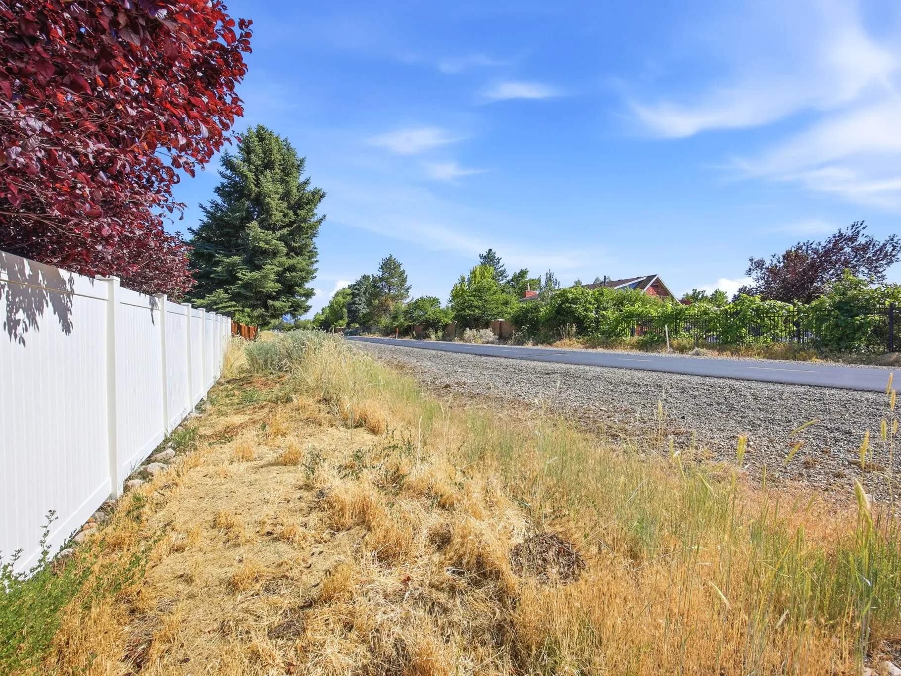 White privacy fence bordering a gravel roadside