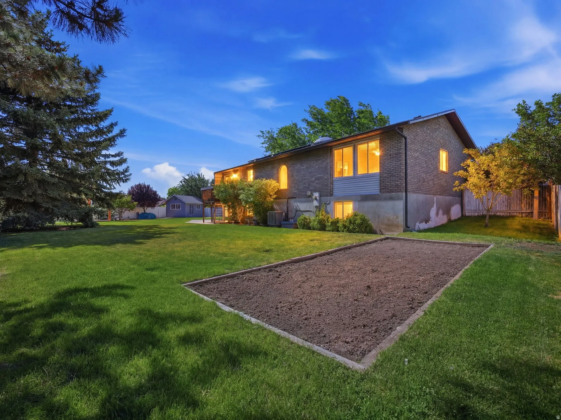 Spacious backyard featuring a large garden bed, mature evergreen trees, and a privacy fence