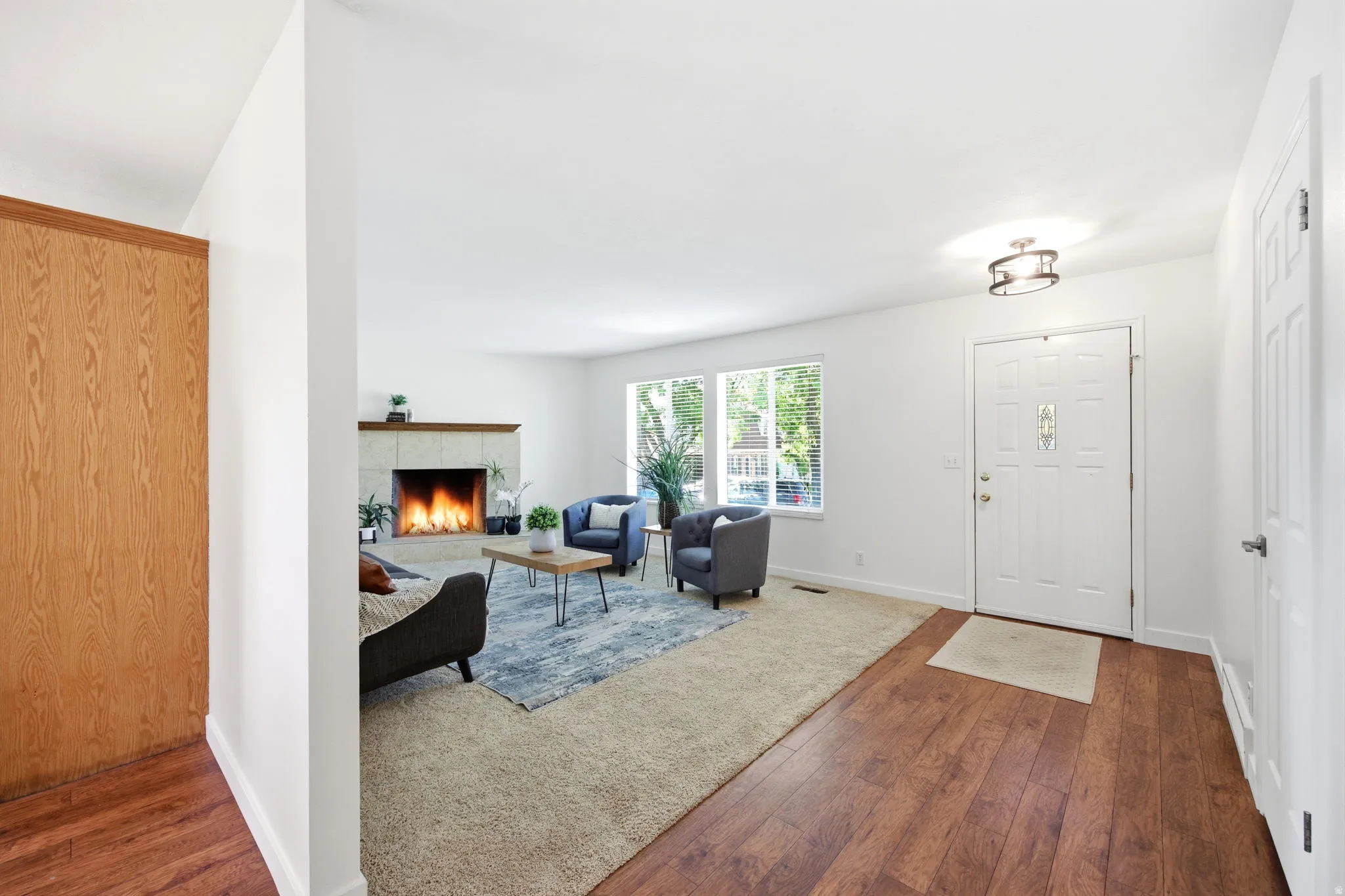 Spacious entryway featuring wood-finish flooring, leading to a living area with a tile-surround fireplace and large windows