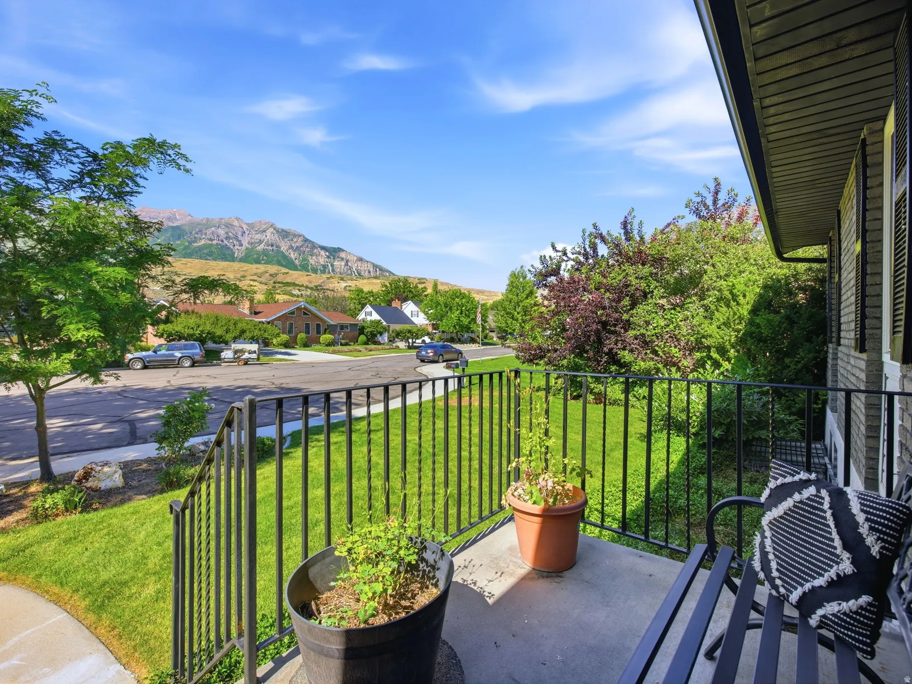 Front porch with black metal railing, brick exterior, and a manicured lawn