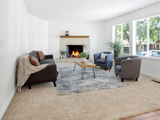 Living area featuring a stone-clad fireplace with a wood mantel, broad windows, and a combination of wood-finish flooring and carpeting