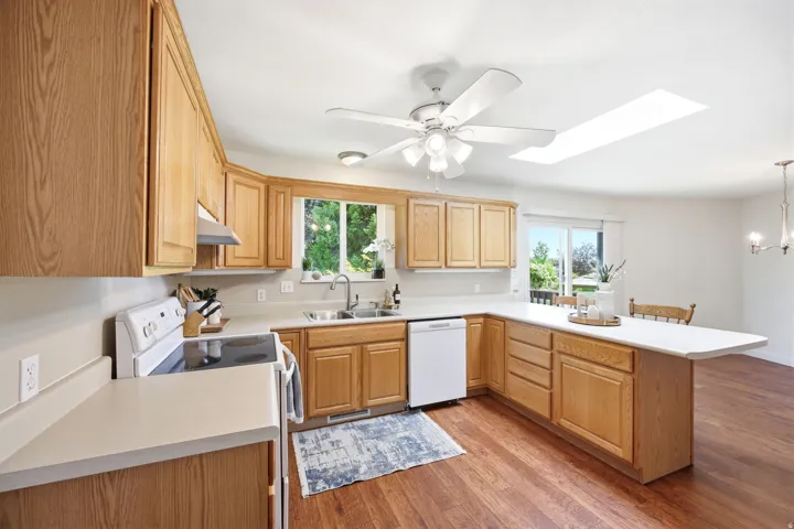 Kitchen featuring wood-finish flooring, wood cabinetry, white countertops, and white appliances