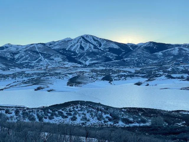 Expansive mountainous landscape featuring snow-covered peaks, a frozen body of water, and a distant ski resort