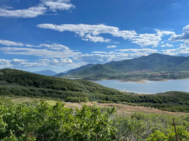 Expansive mountain landscape featuring a large body of water, distant peaks, and scattered residential structures