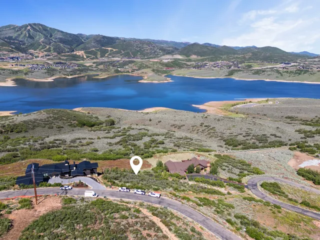 Elevated property featuring a mountain backdrop and a prominent lake, with a winding paved road providing access