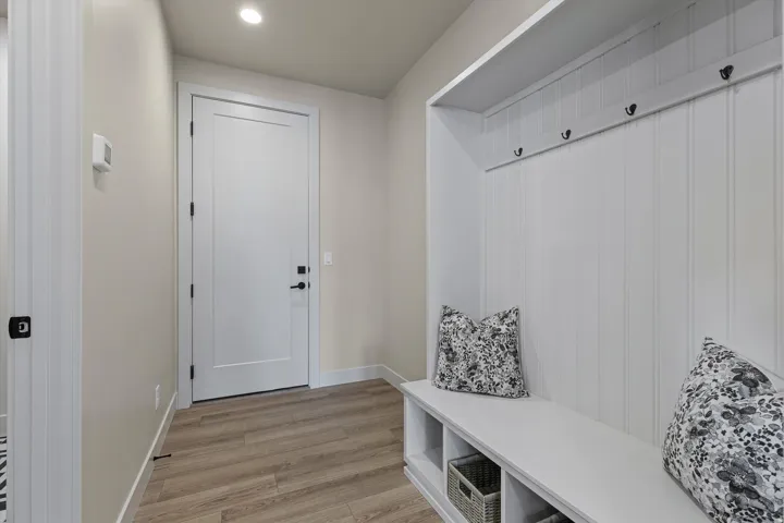 Entryway mudroom featuring wood-finish flooring, a built-in bench with open storage cubbies, beadboard paneling, and matte black coat hooks