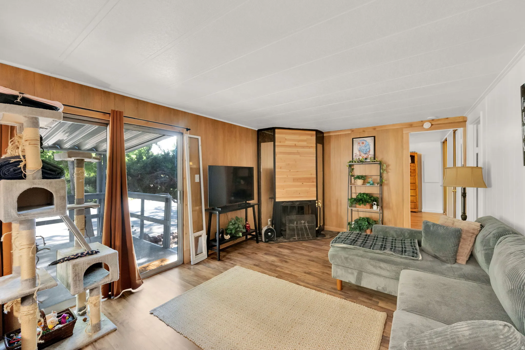 Living area featuring wood-finish flooring, wood paneling, a corner fireplace with wood surround, and sliding glass doors opening to an exterior deck