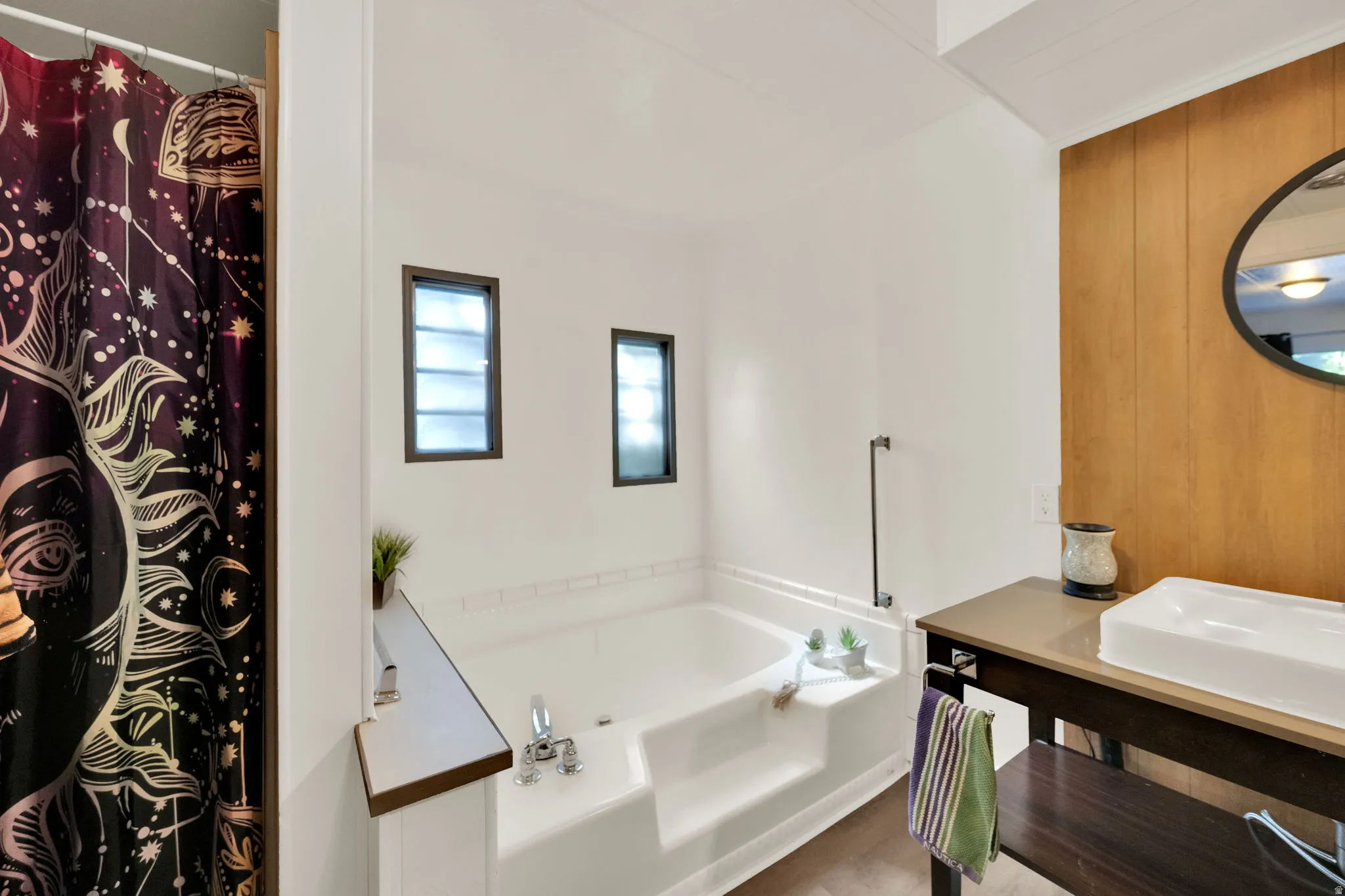 Master Bathroom featuring a built-in soaking tub with steps, two frosted windows, and a wood-finish accent wall