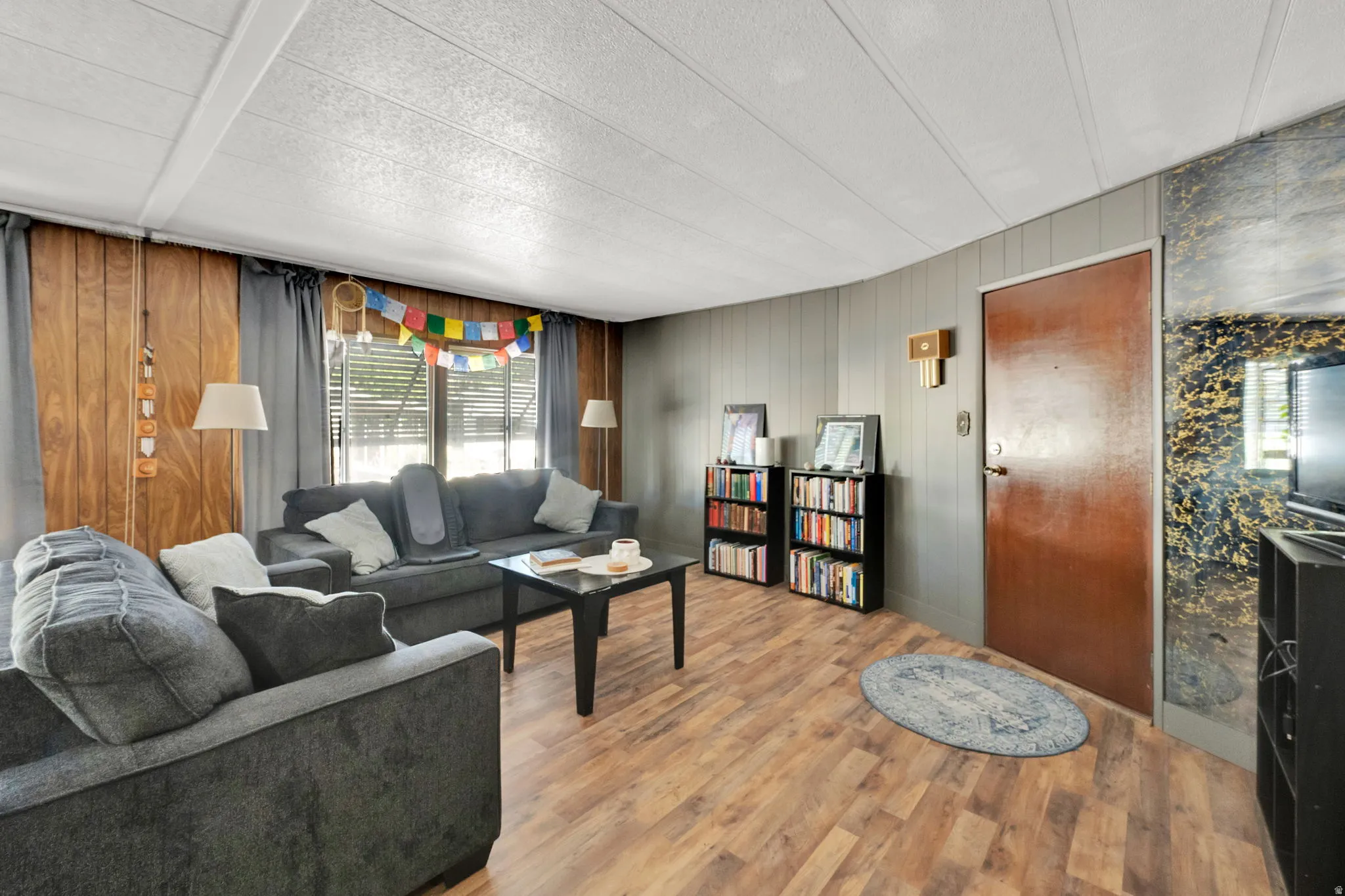 Living area featuring wood-finish flooring, paneled walls, and a white panel ceiling