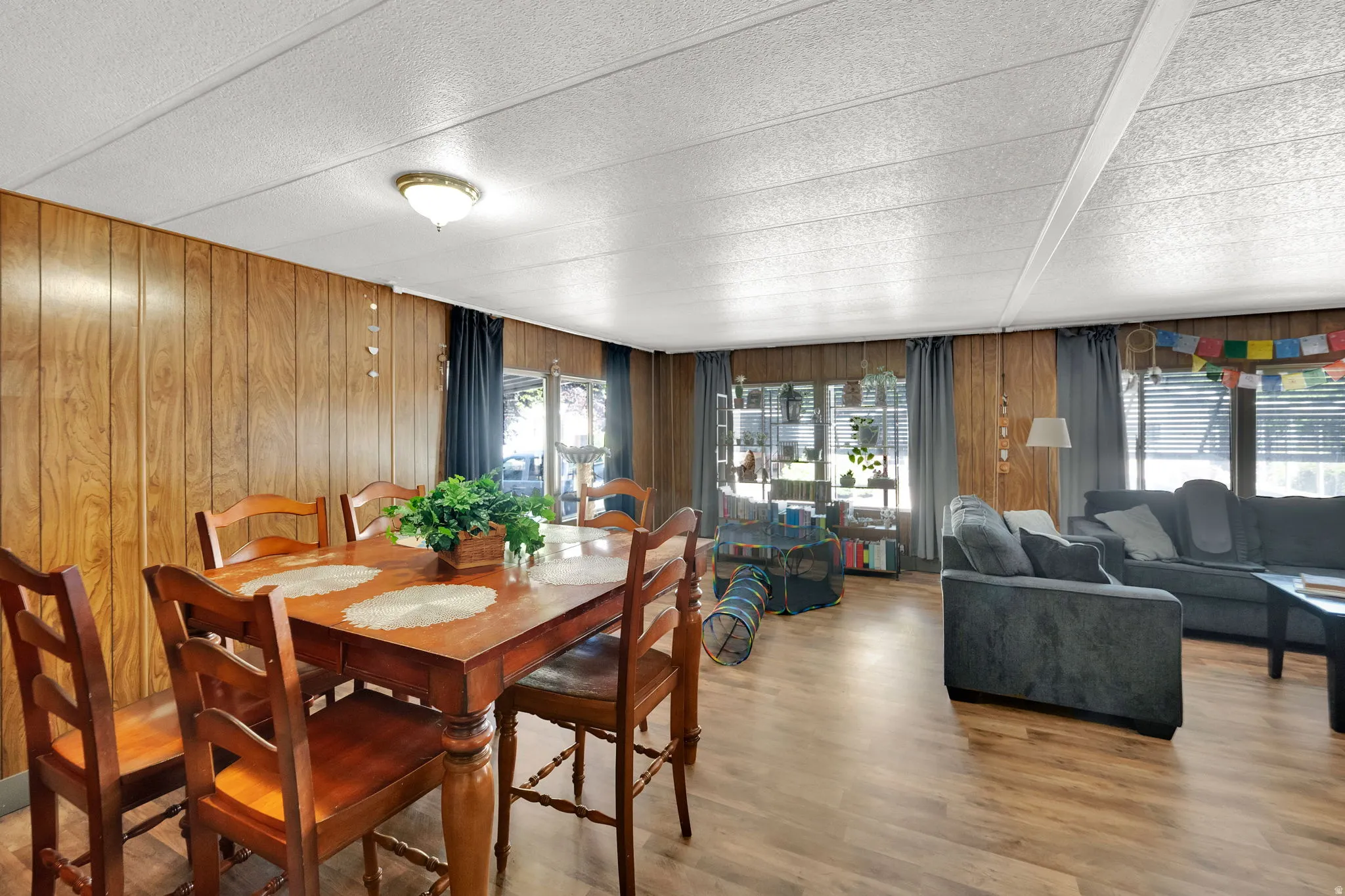Open-concept living space featuring wood-finish paneling, wood-finish flooring, and multiple windows with blinds