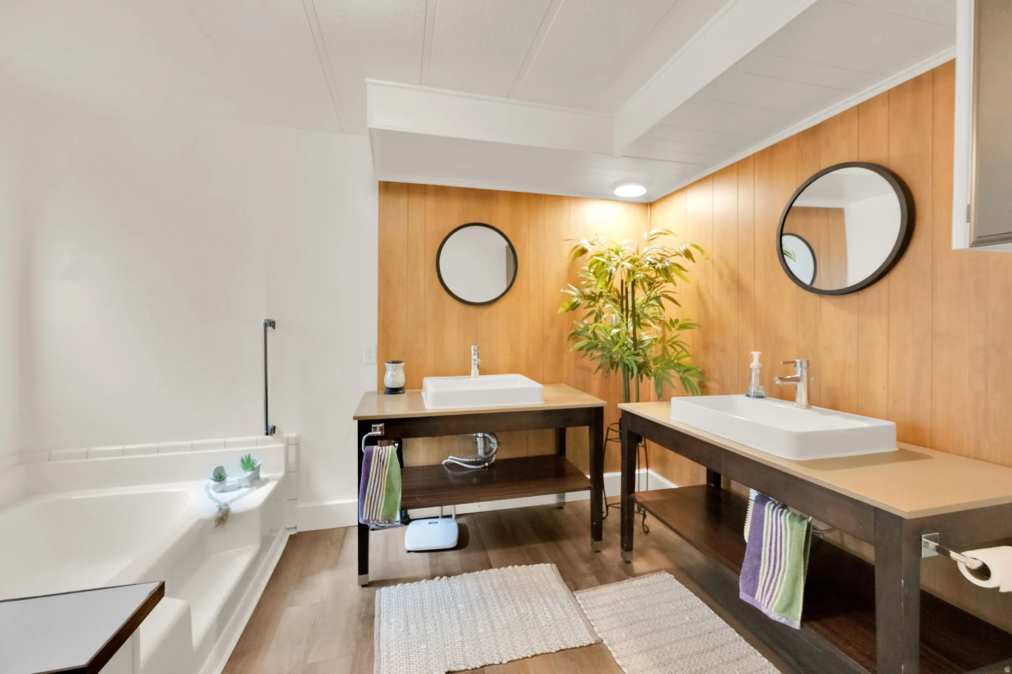 Master Bathroom featuring a soaking tub, dual vessel sinks, wood-finish flooring, and wood paneling accents