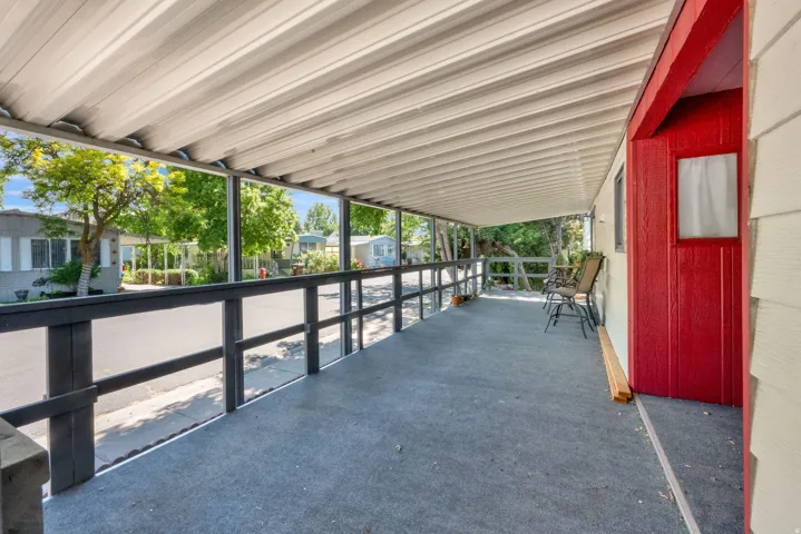 Covered porch featuring a metal roof, dark-stained railing, and a red entry door with a small window