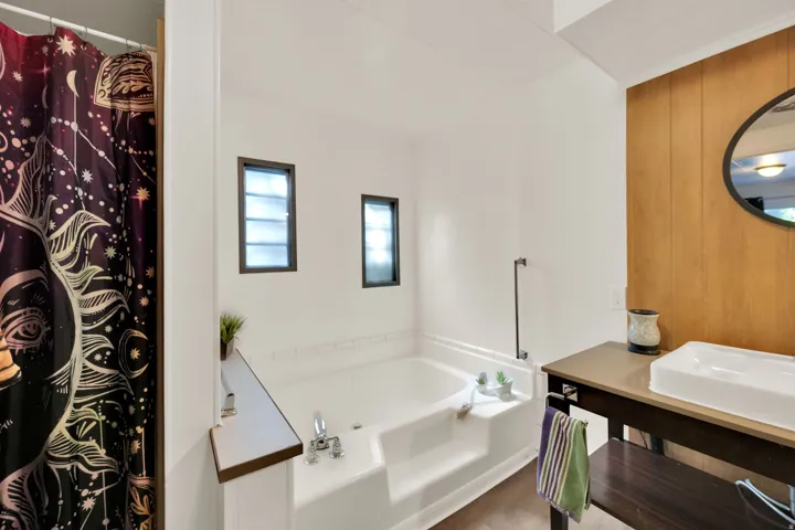 Master Bathroom featuring a built-in soaking tub with steps, two frosted windows, and a wood-finish accent wall