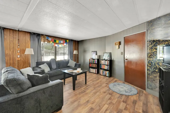 Living area featuring wood-finish flooring, paneled walls, and a white panel ceiling