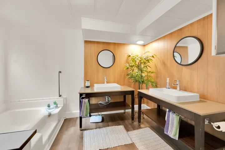 Master Bathroom featuring a soaking tub, dual vessel sinks, wood-finish flooring, and wood paneling accents