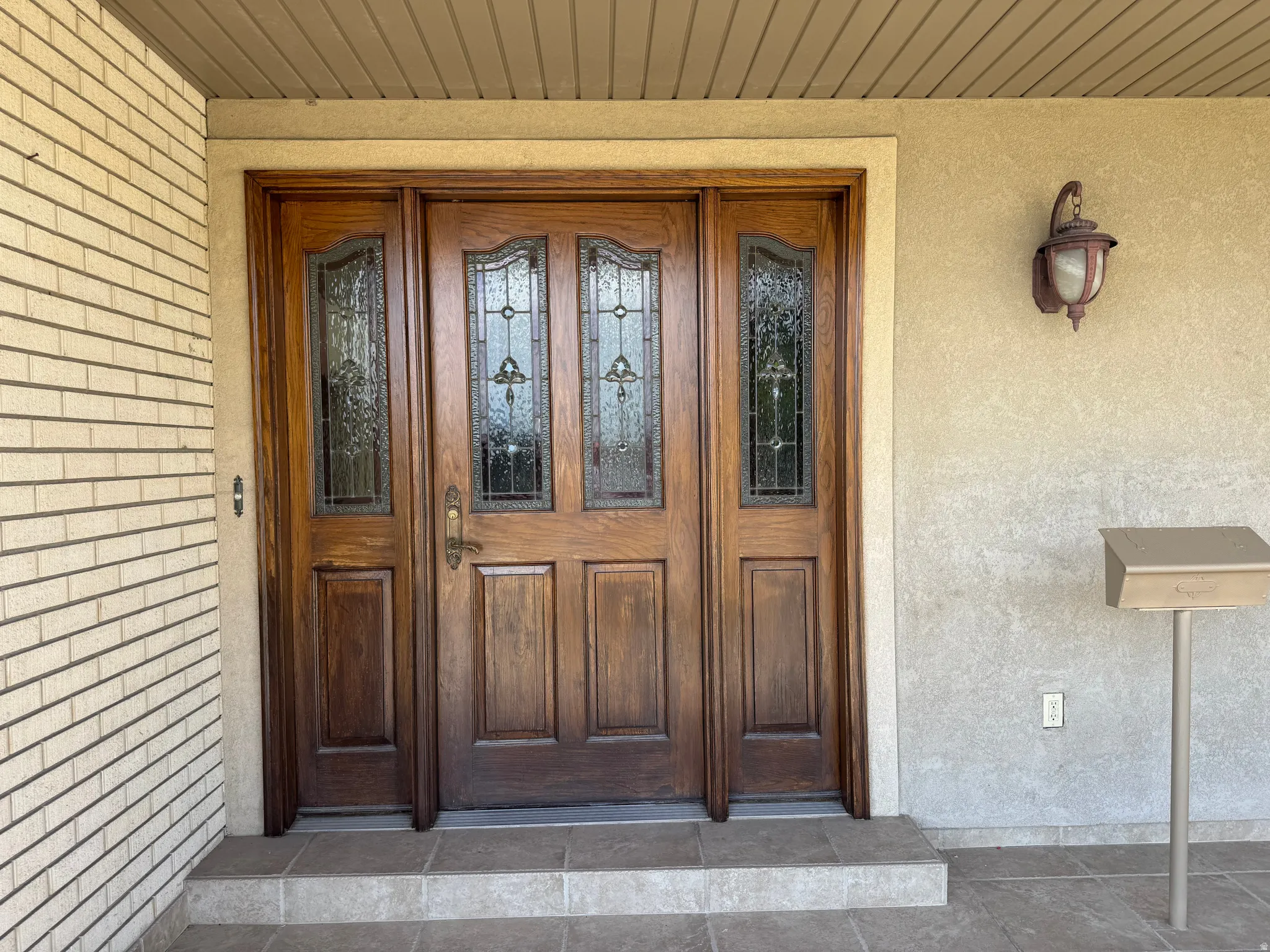 Rich wood-finish entry door with decorative glass inserts and sidelights