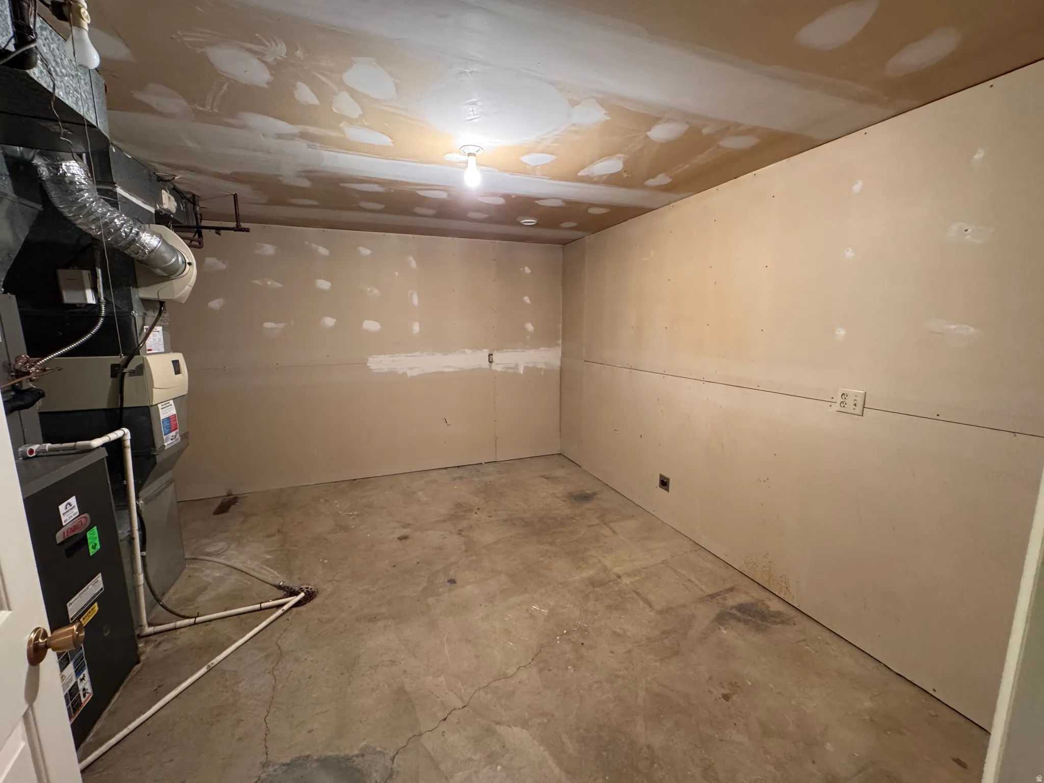 Unfinished space featuring concrete flooring, unpainted drywall walls, and an exposed ceiling with a single light fixture