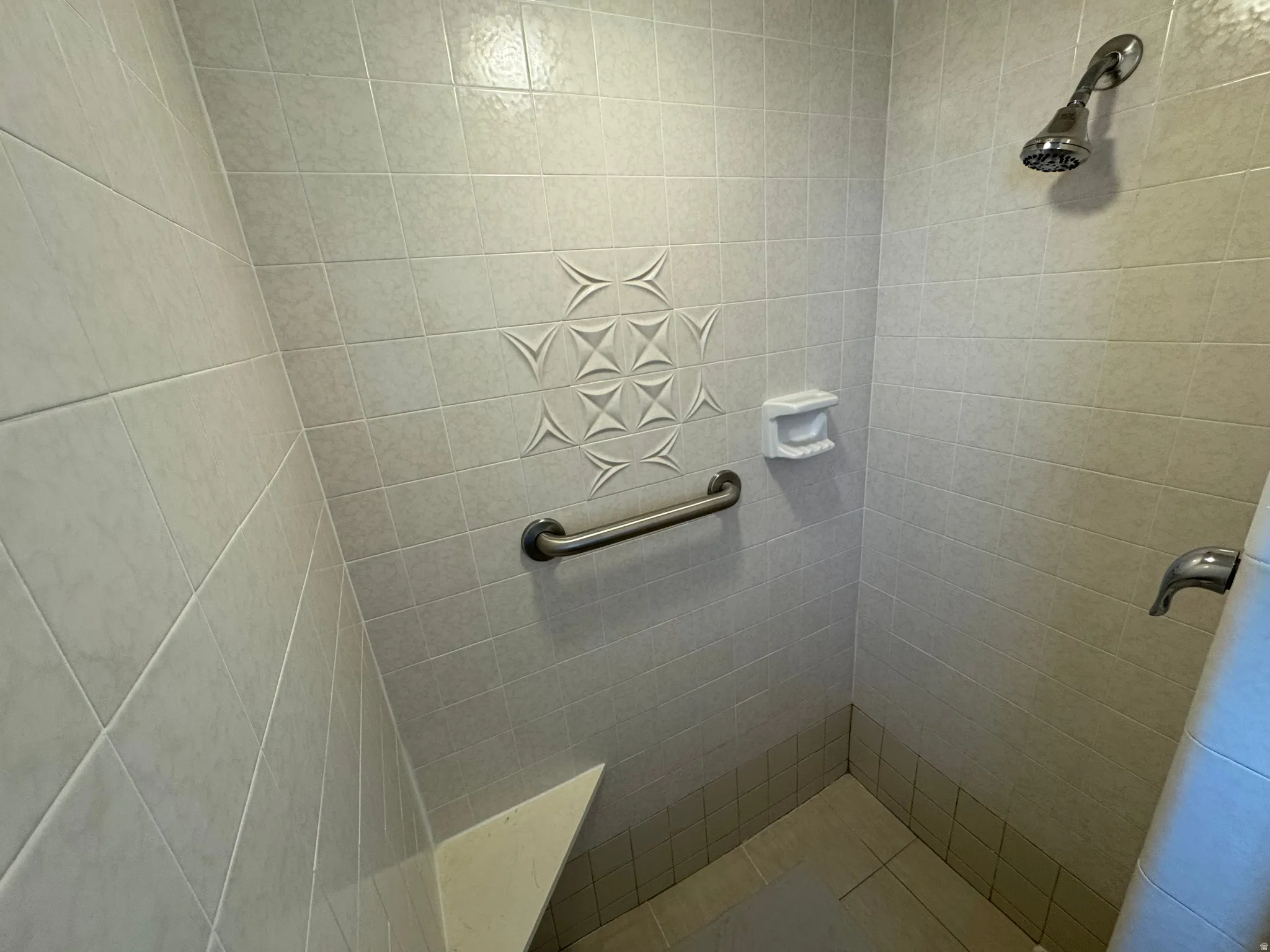 Tiled shower enclosure featuring a built-in bench, decorative accent tiles, a grab bar, and a chrome shower head and faucet