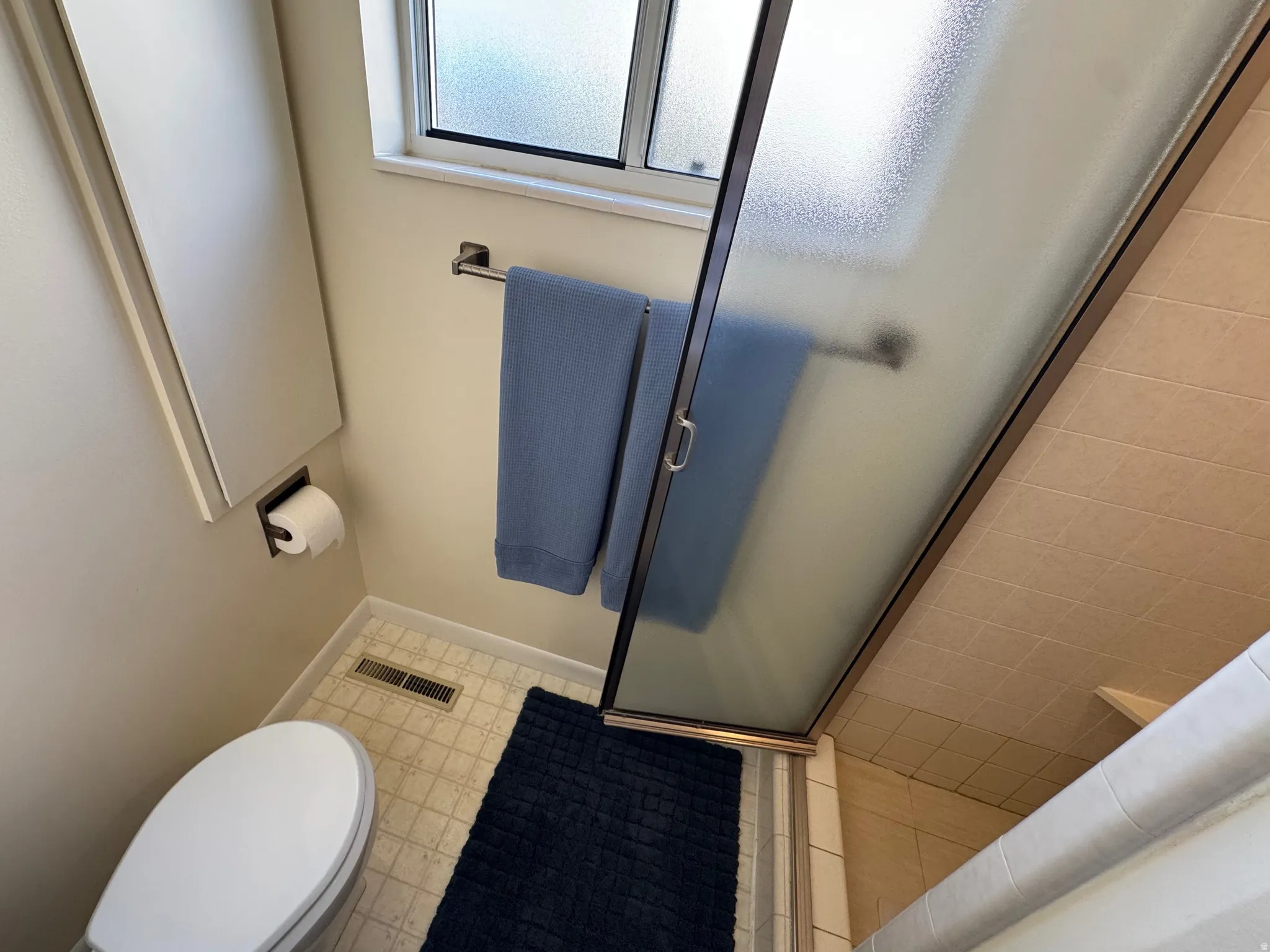 Compact bathroom featuring a white toilet, frosted glass window, and a shower with a sliding door