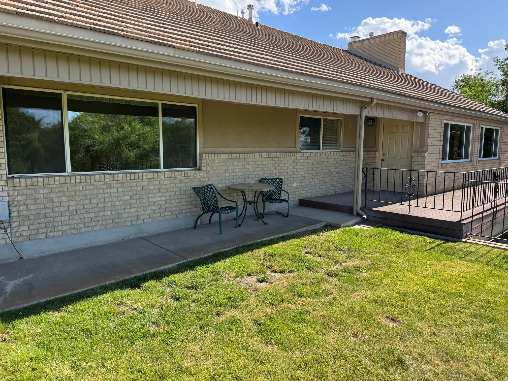 Exterior brick facade with multiple windows, a composite deck featuring a black metal railing, and a concrete patio