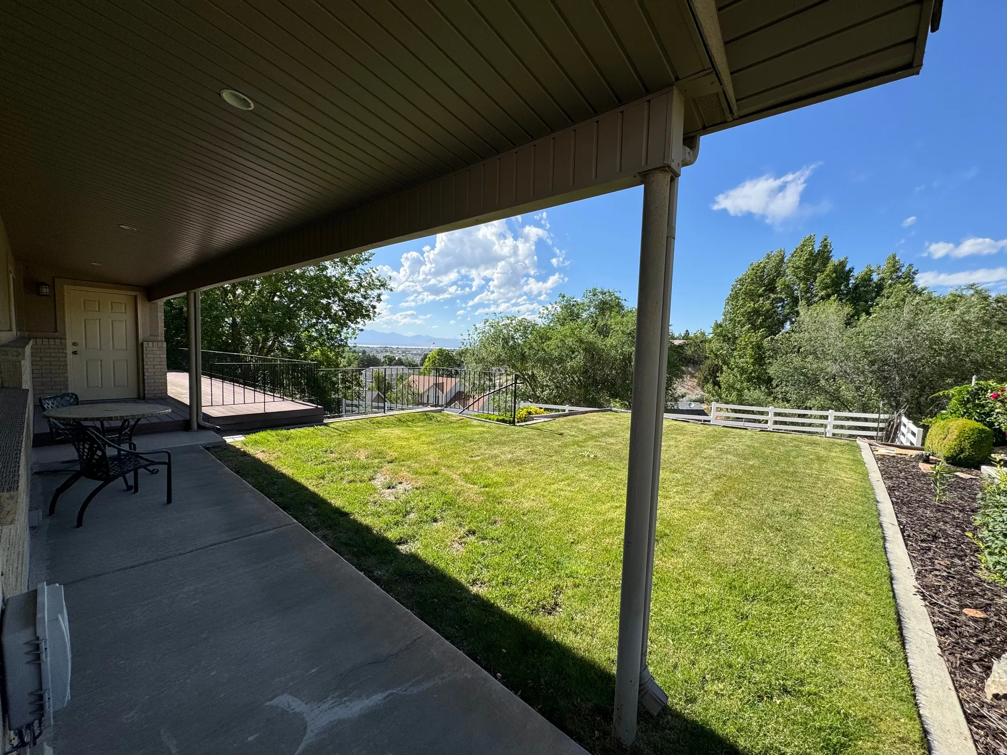Covered concrete patio extending to a wooden deck with metal railing
